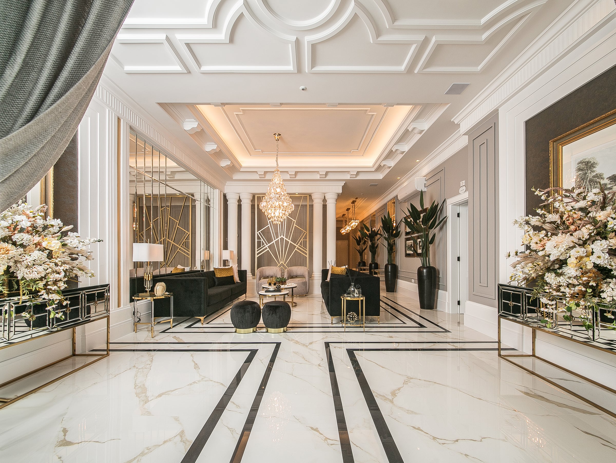 Corredor do lobby do Noah, com piso de mármore, colunas clássicas e lustre de cristal